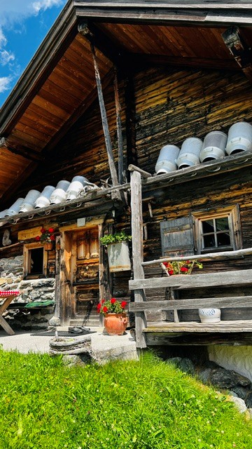 Almhaus mit alten Milchkannen an der Fassade, blaue Fensterläden